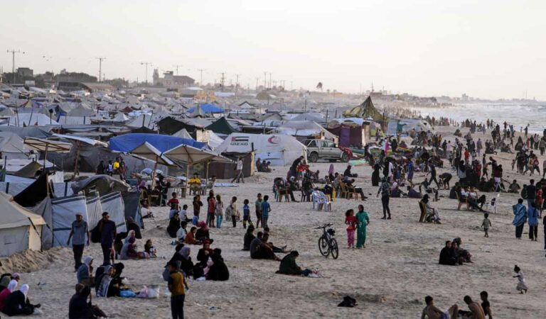 Displaced Palestinians walk through a tent camp in Muwasi, an area that Israel has designated as a safe zone, in Khan Younis southern Gaza Strip