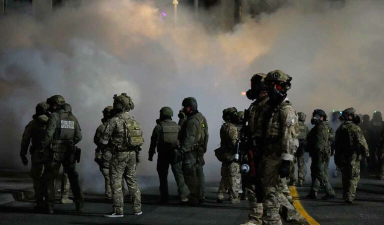 Law enforcement officers stand in tear gas outside a US Immigration and Customs Enforcement facility during a protest in Portland.